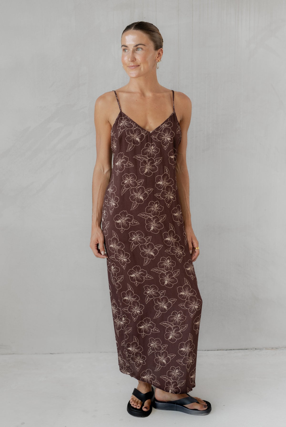 Woman wearing a long brown floral dress against a plain background