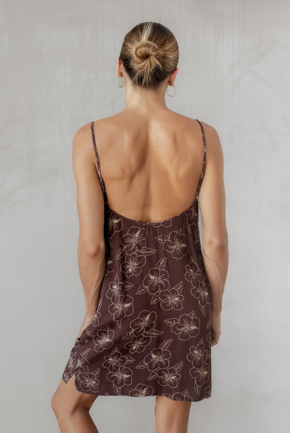 Woman wearing a brown floral dress with thin straps on a plain background