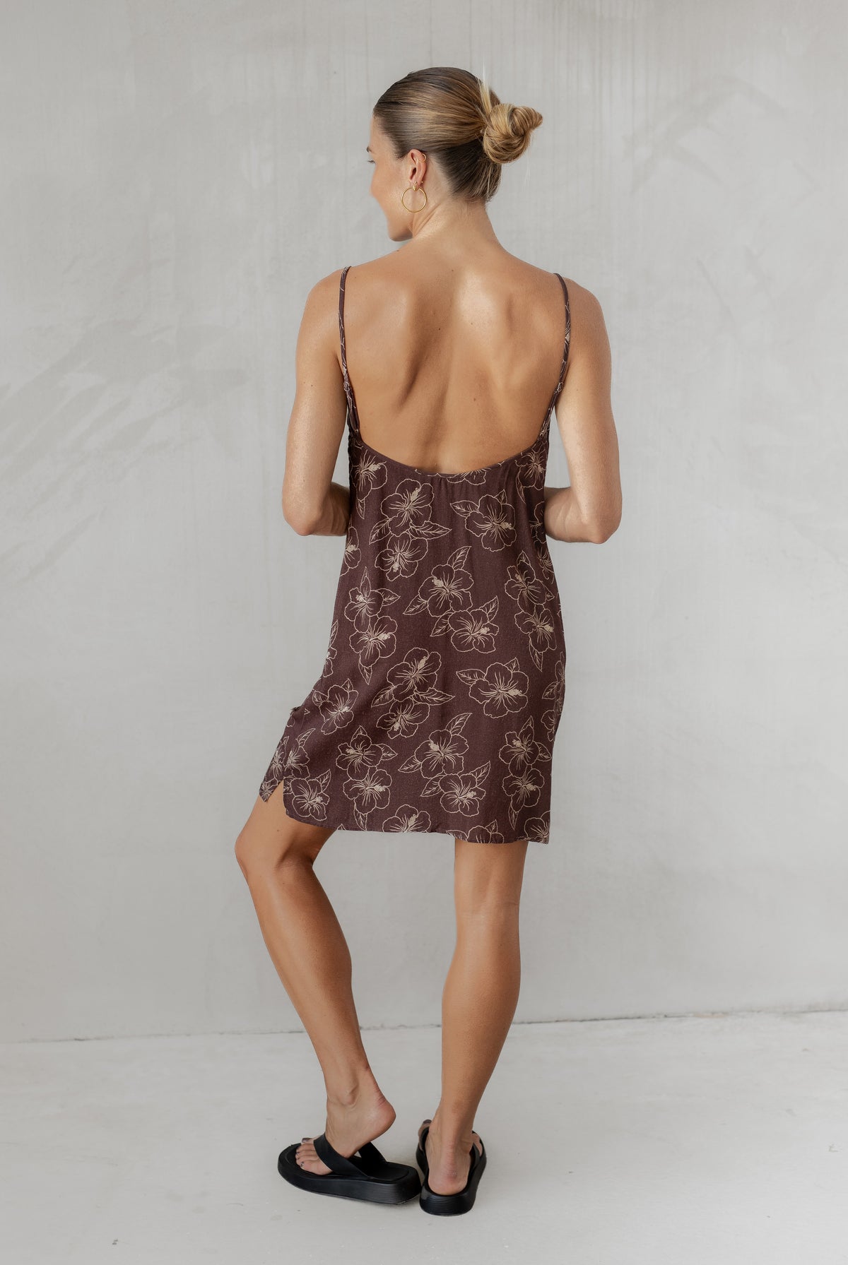 Woman wearing a brown patterned dress with thin straps on a plain background