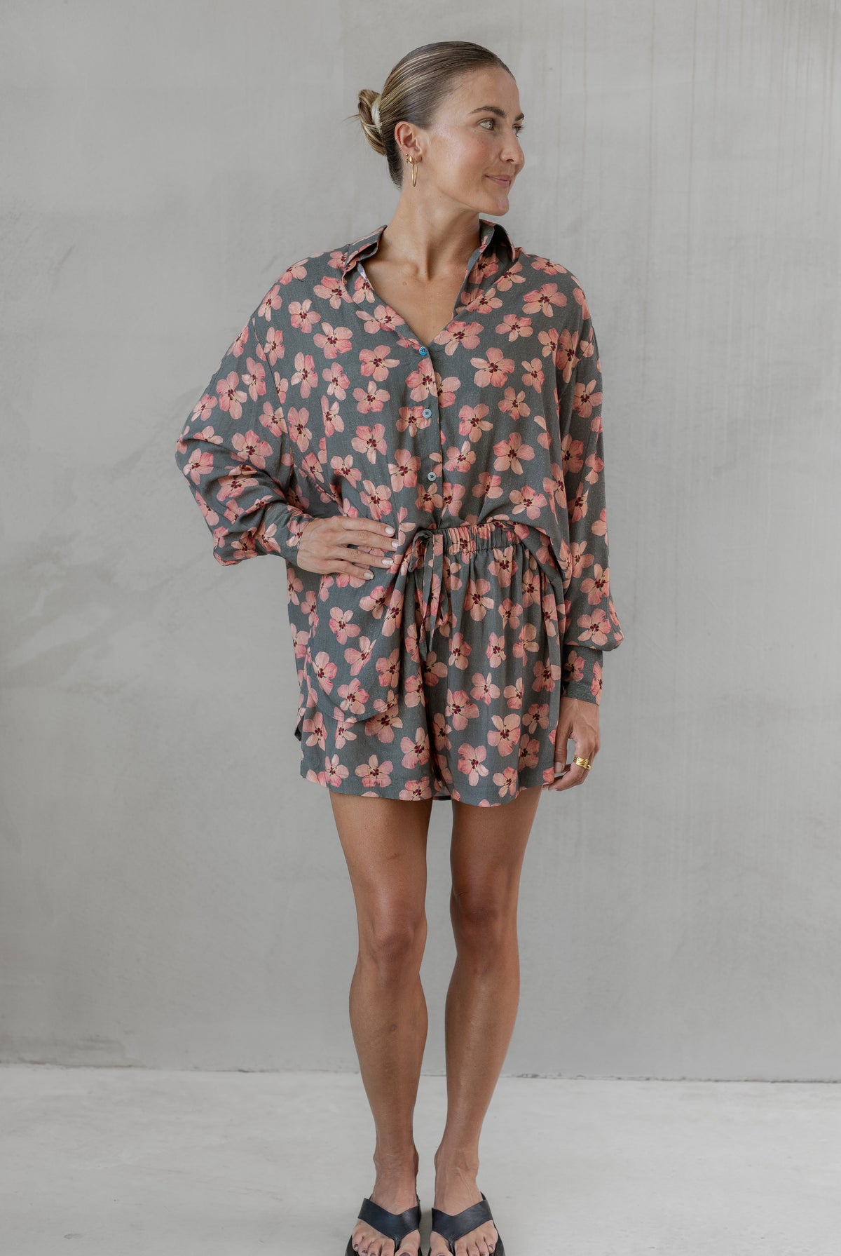 Woman wearing a gray and pink floral shirt with matching shorts against a plain background