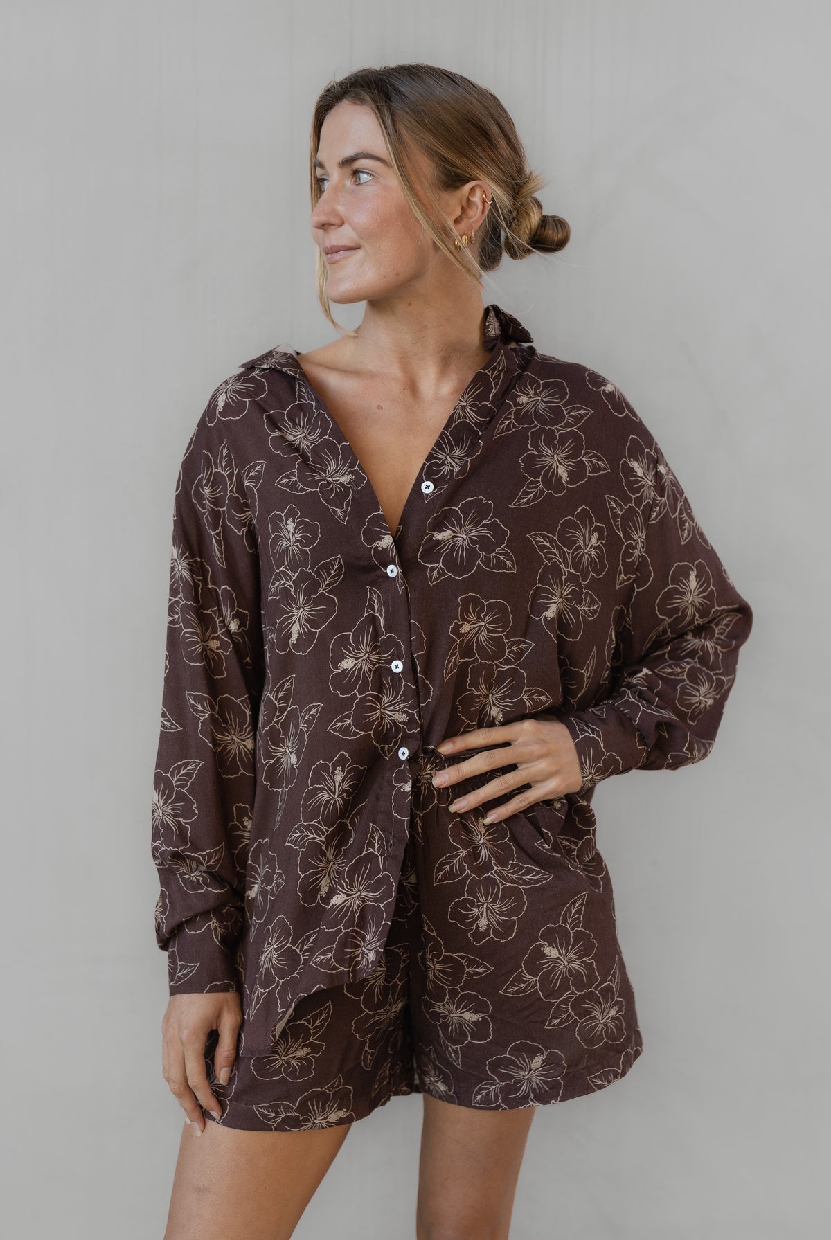 Woman wearing a brown floral patterned shirt with matching shorts against a plain background
