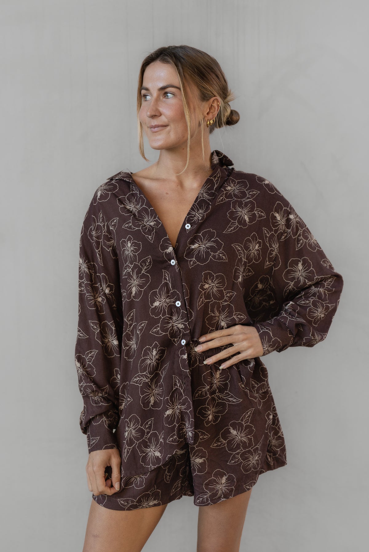Woman wearing a brown floral patterned shirt with matching shorts against a plain background