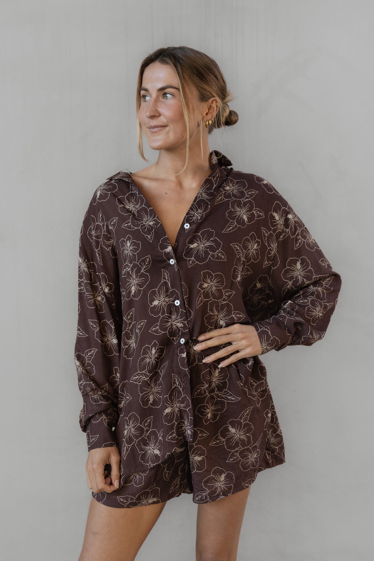 Woman wearing a brown floral patterned shirt with matching shorts against a plain background
