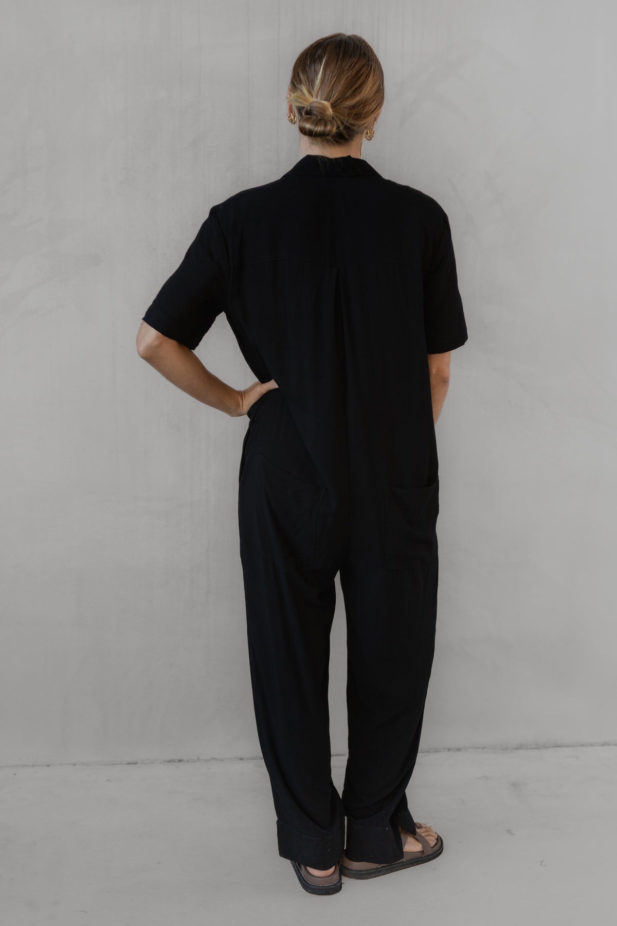 Person wearing a black jumpsuit against a plain background