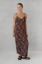 Woman wearing a long brown floral dress against a plain background