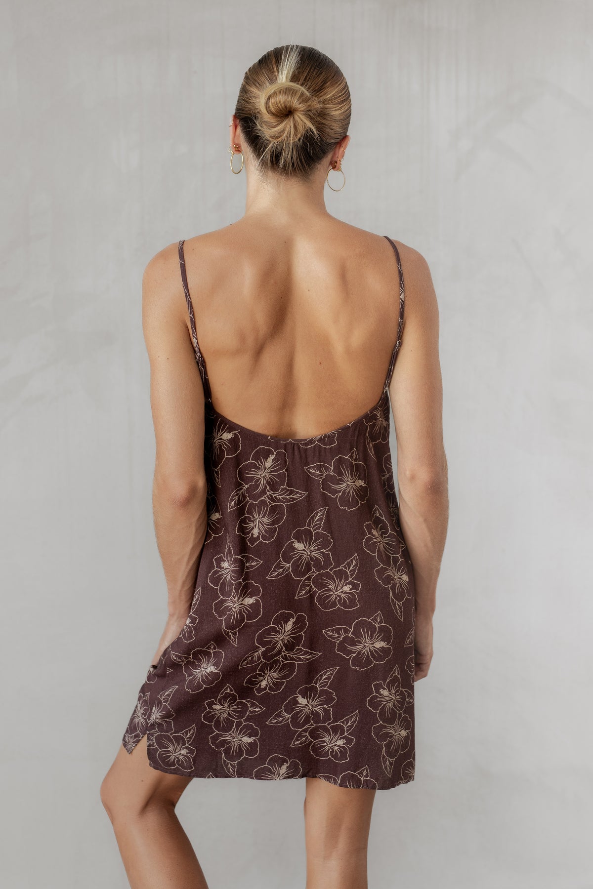 Woman wearing a brown floral dress with thin straps on a plain background