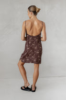 Woman wearing a brown patterned dress with thin straps on a plain background