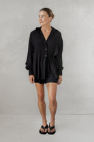 Woman wearing a black shirt with matching shorts against a plain background