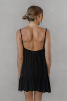 Woman wearing a black dress with thin straps against a plain background