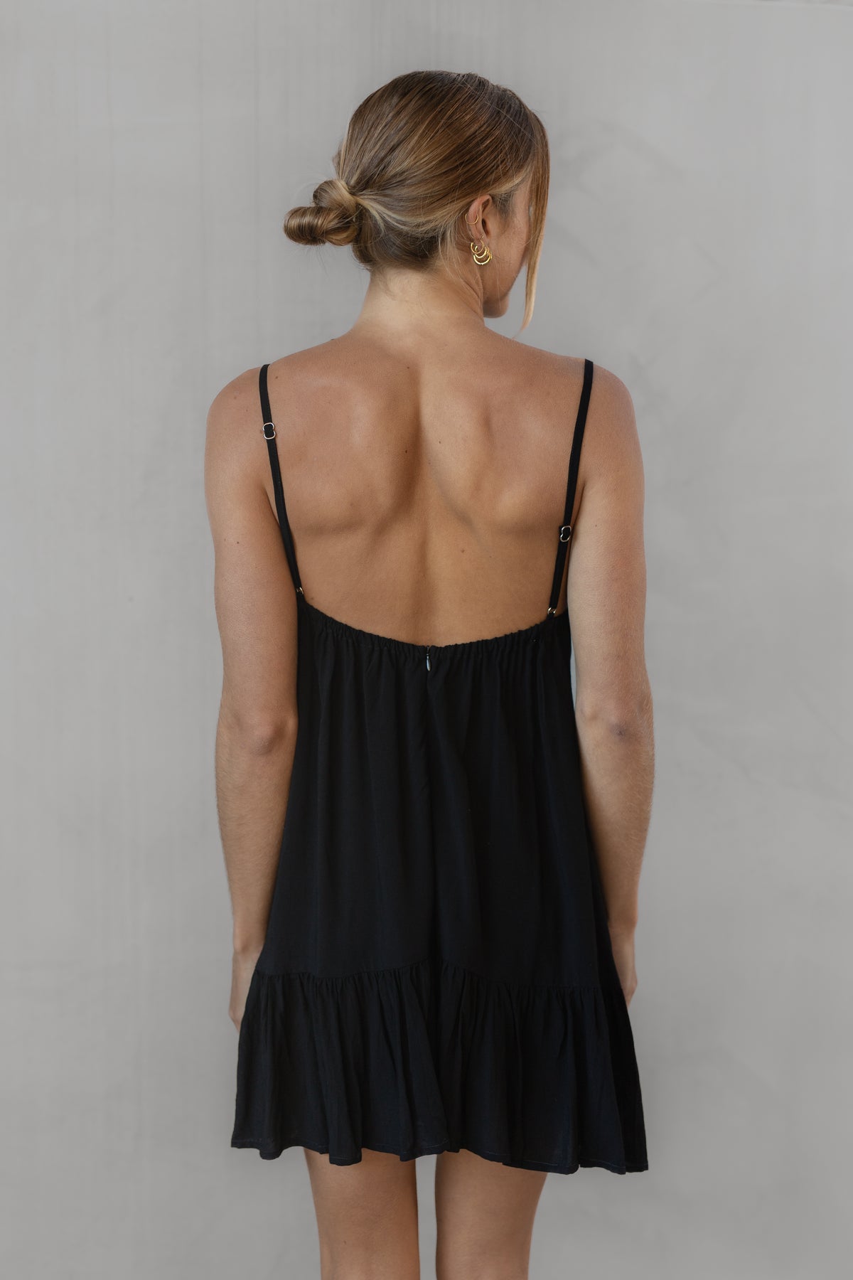 Woman wearing a black dress with thin straps against a plain background