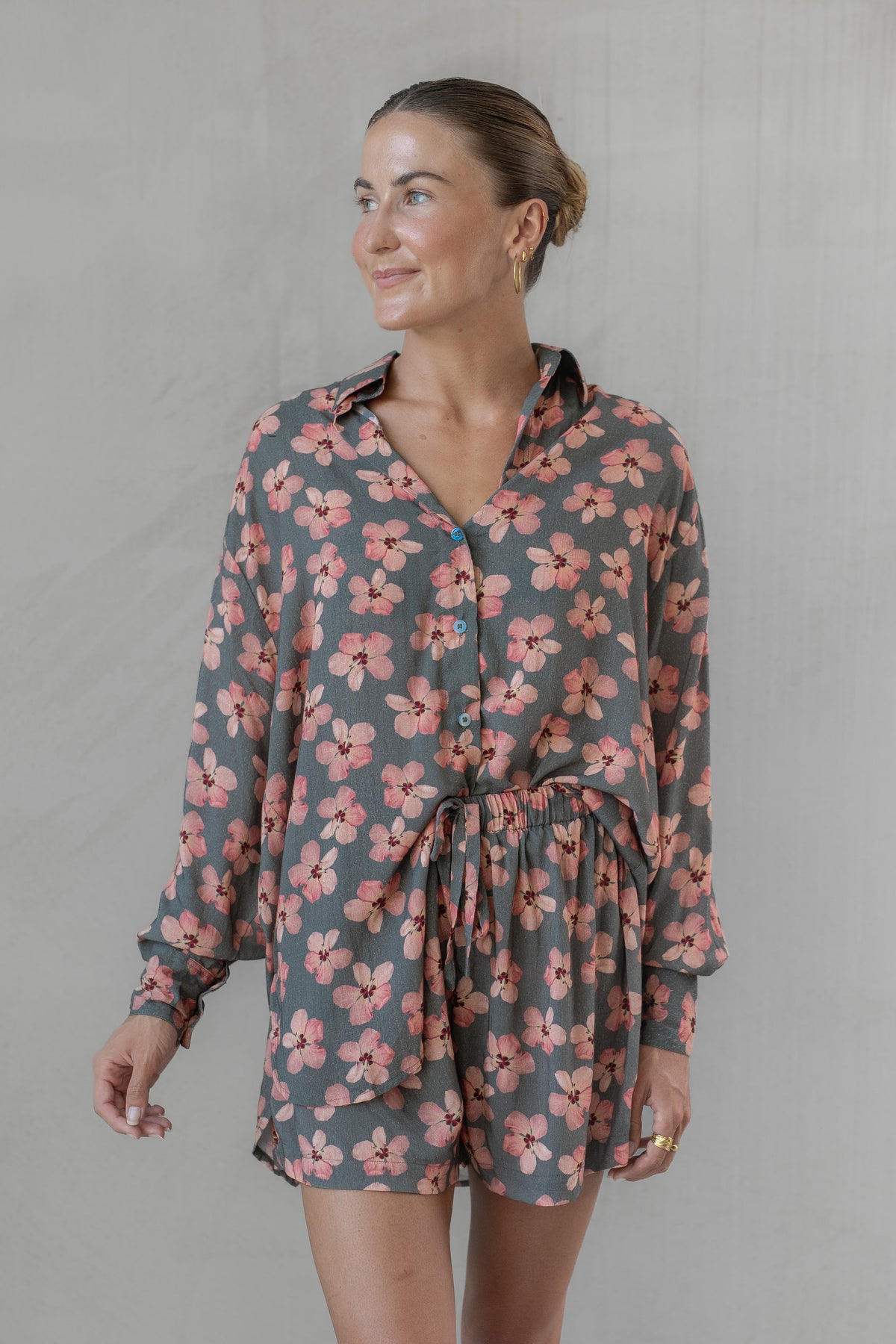 Woman wearing a gray and pink floral shirt with matching shorts against a plain background