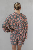 Woman wearing a gray and pink floral shirt with matching shorts against a neutral background