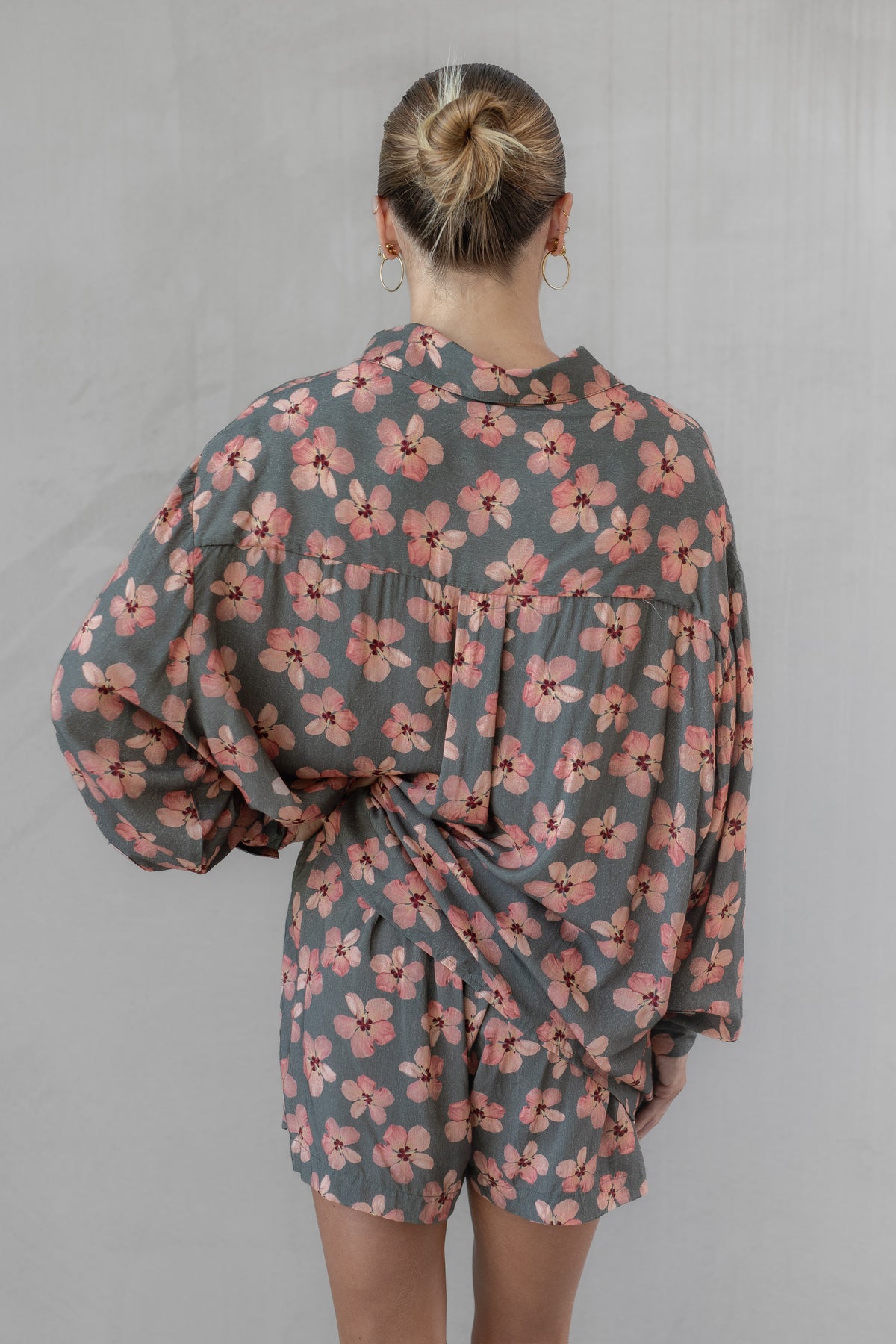Woman wearing a gray and pink floral shirt with matching shorts against a neutral background