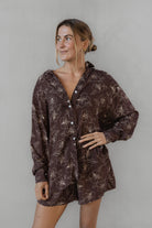 Woman wearing a brown floral patterned shirt with matching shorts against a plain background